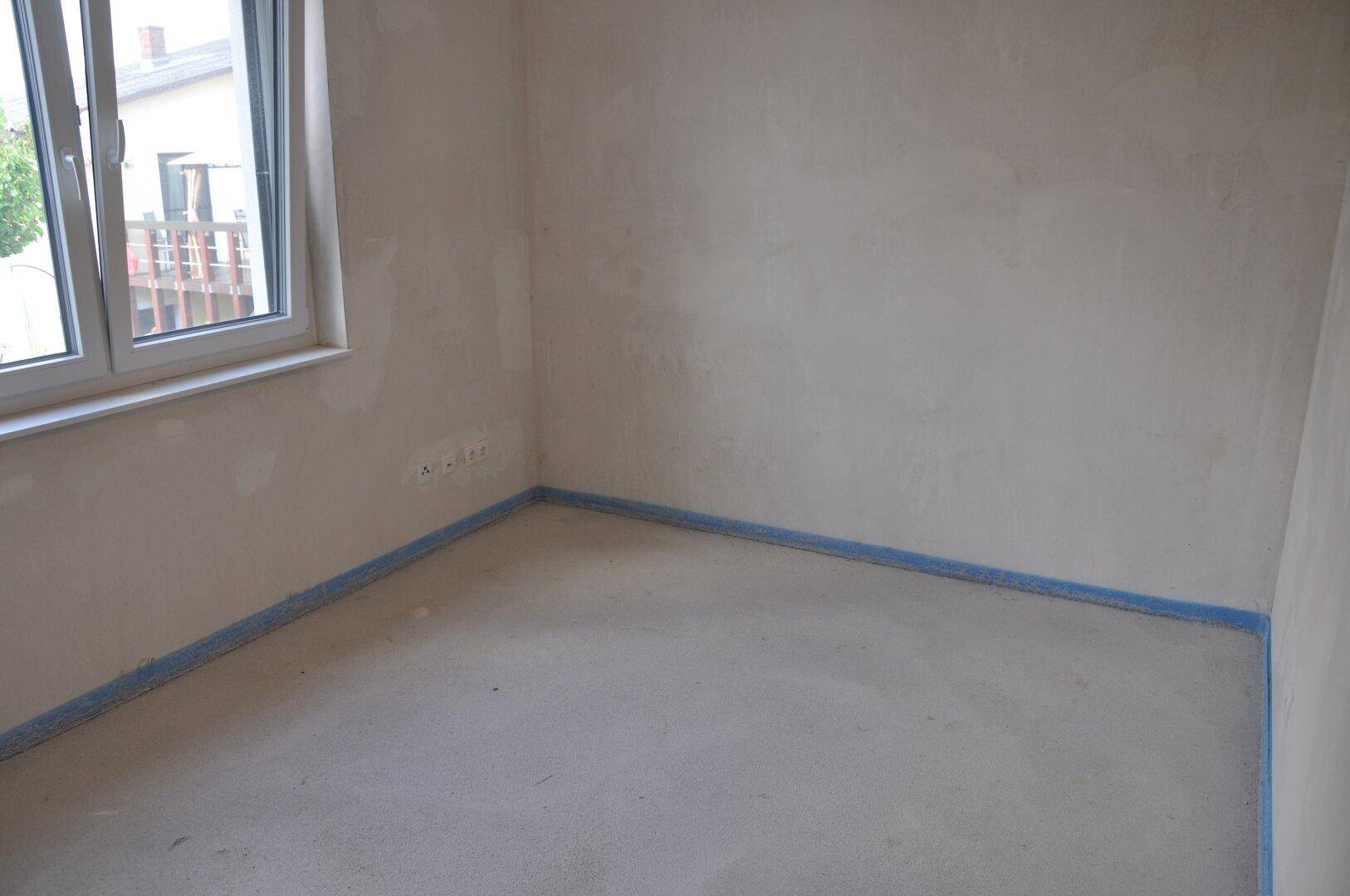 Unfertiges Schlafzimmer mit Fenster und Rohbauwänden, bereit für den Innenausbau.