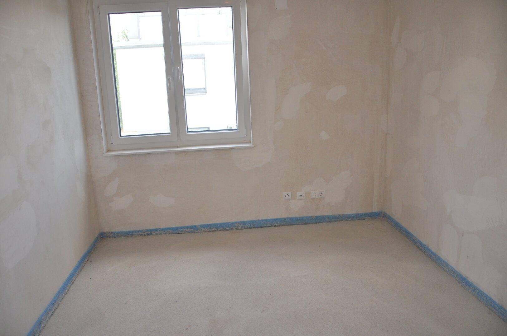 Unfertiges Zimmer mit Fenster und Rohbauwänden, wartet auf den finalen Ausbau.