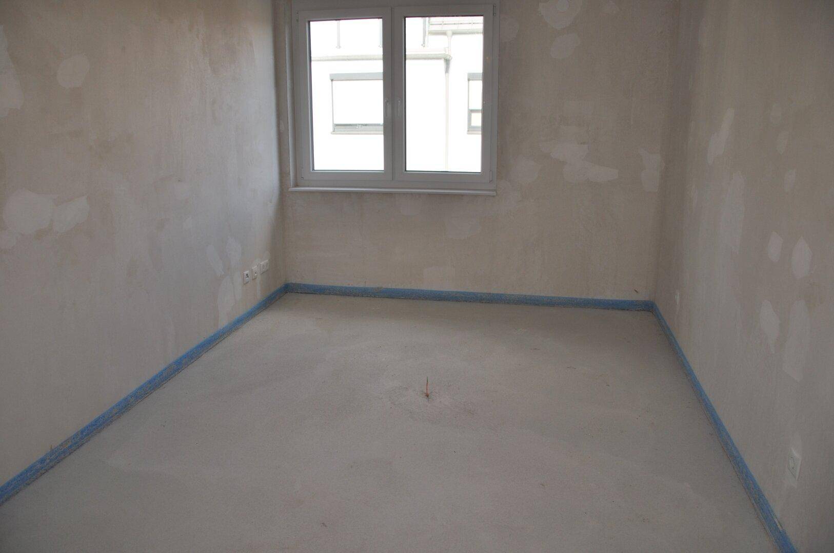 Unfertiges Zimmer mit Fenster und Rohbauwänden, bereit für die individuelle Gestaltung.