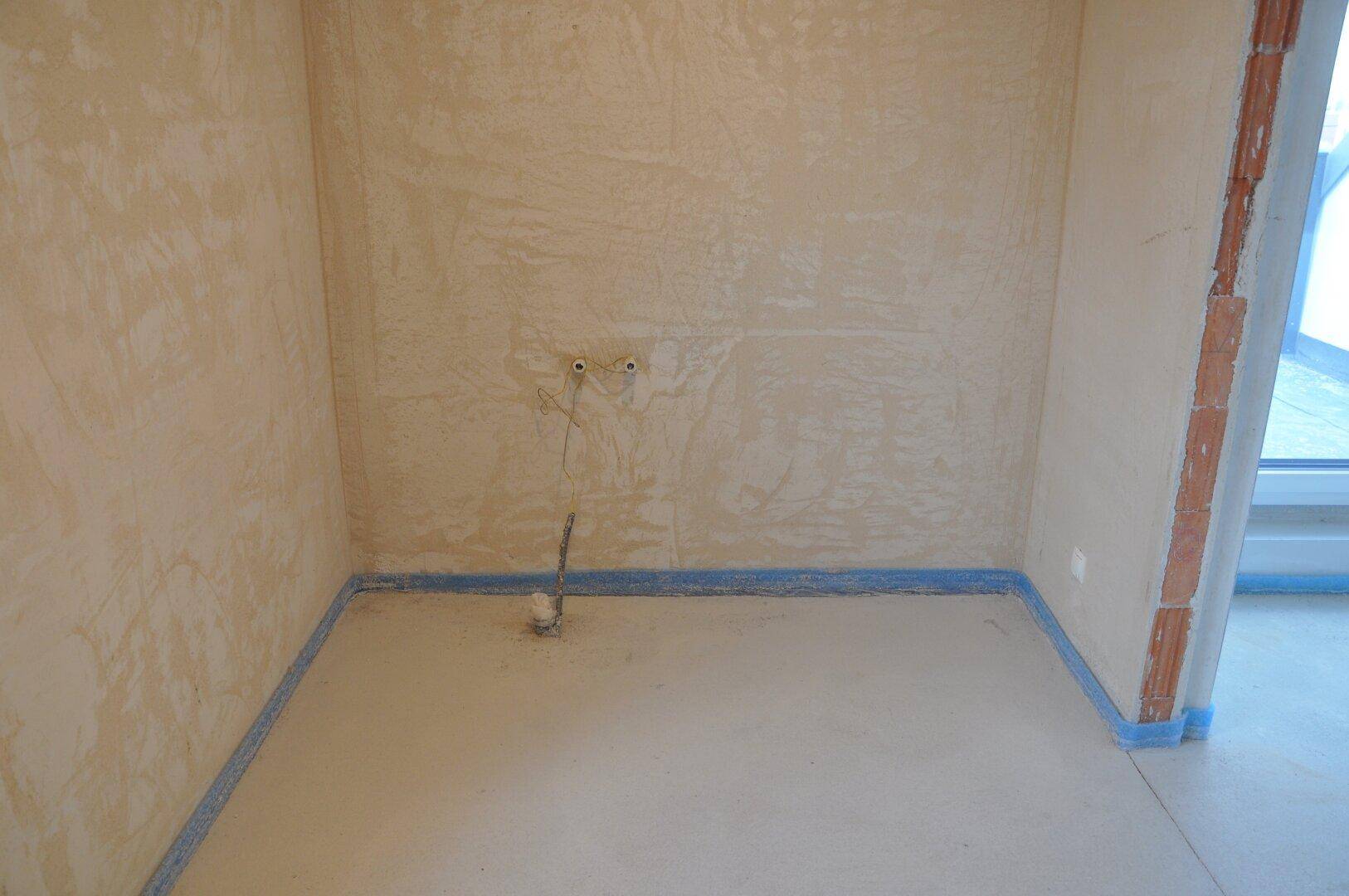 Unfertige Küche mit vorbereiteten Wasseranschlüssen und Rohbauwänden, bereit für die Installation.