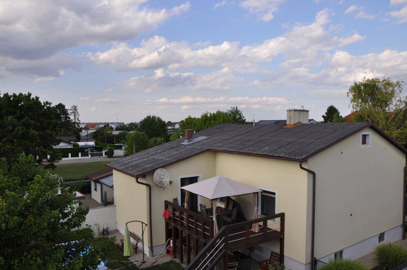Blick auf ein älteres Haus mit gelber Fassade, Holzterrasse und weitem Blick auf die Landschaft und Wasser.