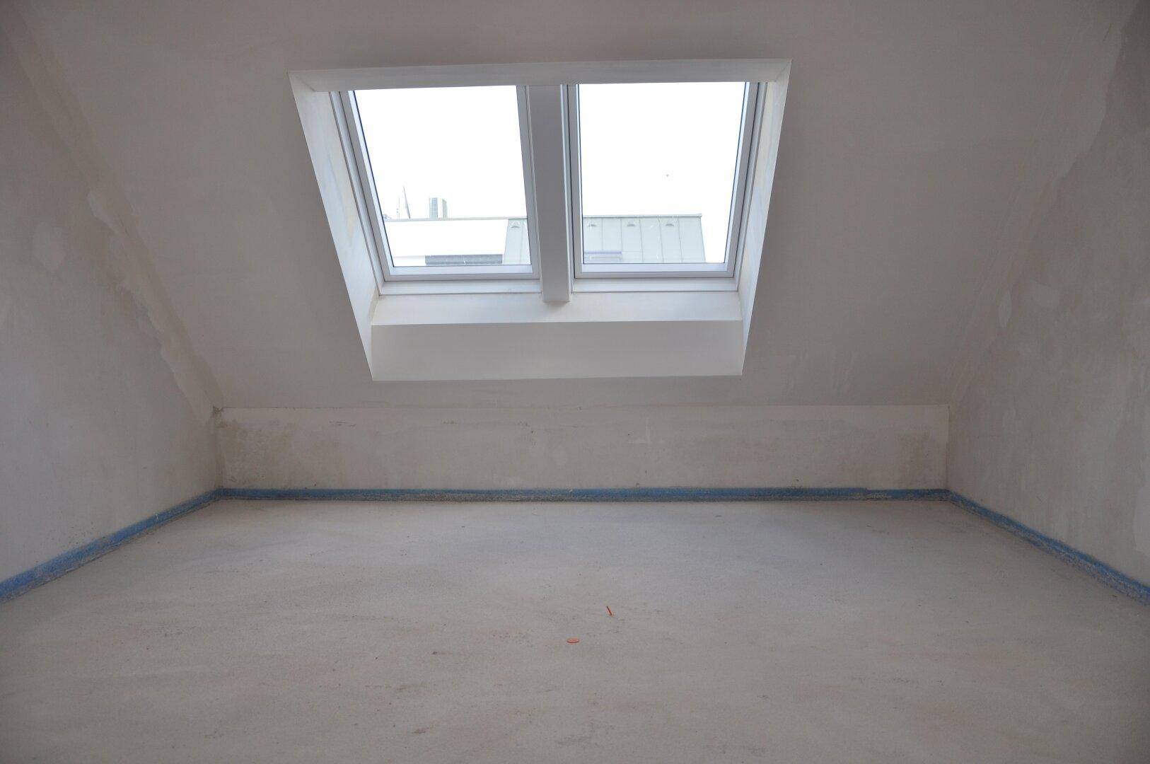 Unfertiges Dachzimmer mit schräger Decke und zwei Dachfenstern, bietet viel natürliches Licht.