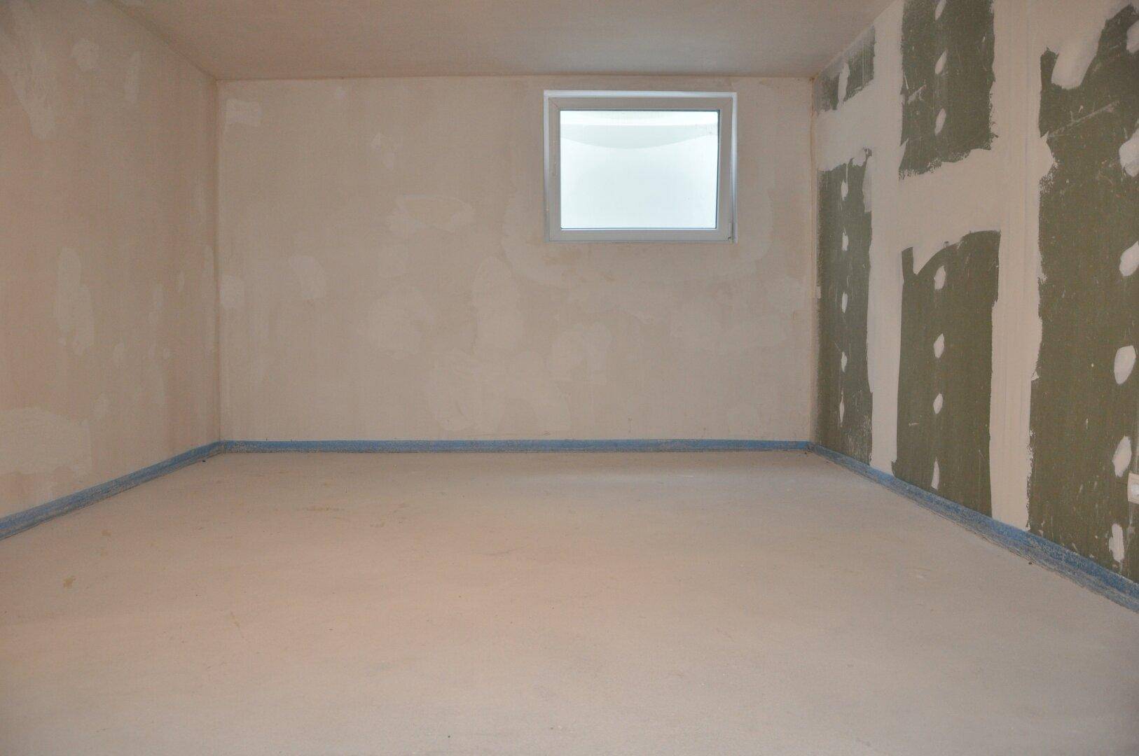 Unfertiger Kellerraum mit kleinem Fenster und Trockenbauwänden, bereit für den weiteren Ausbau.