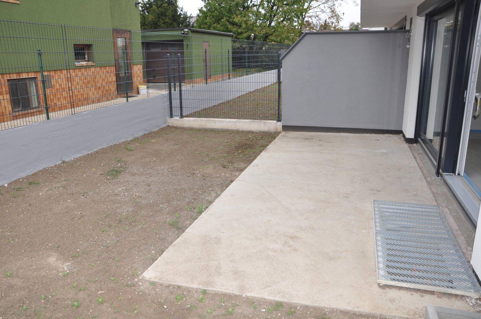 Unfertige Terrasse mit angrenzendem Gartenbereich und Schiebetür zum Innenraum.