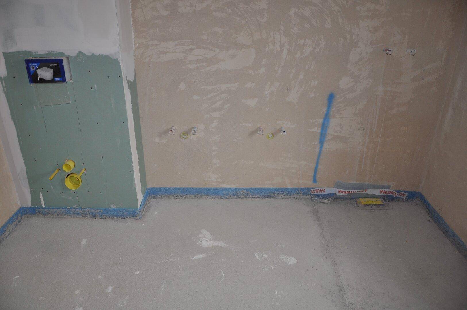Unfertiges WC mit vorbereiteten Anschlüssen für Toilette und Waschbecken.