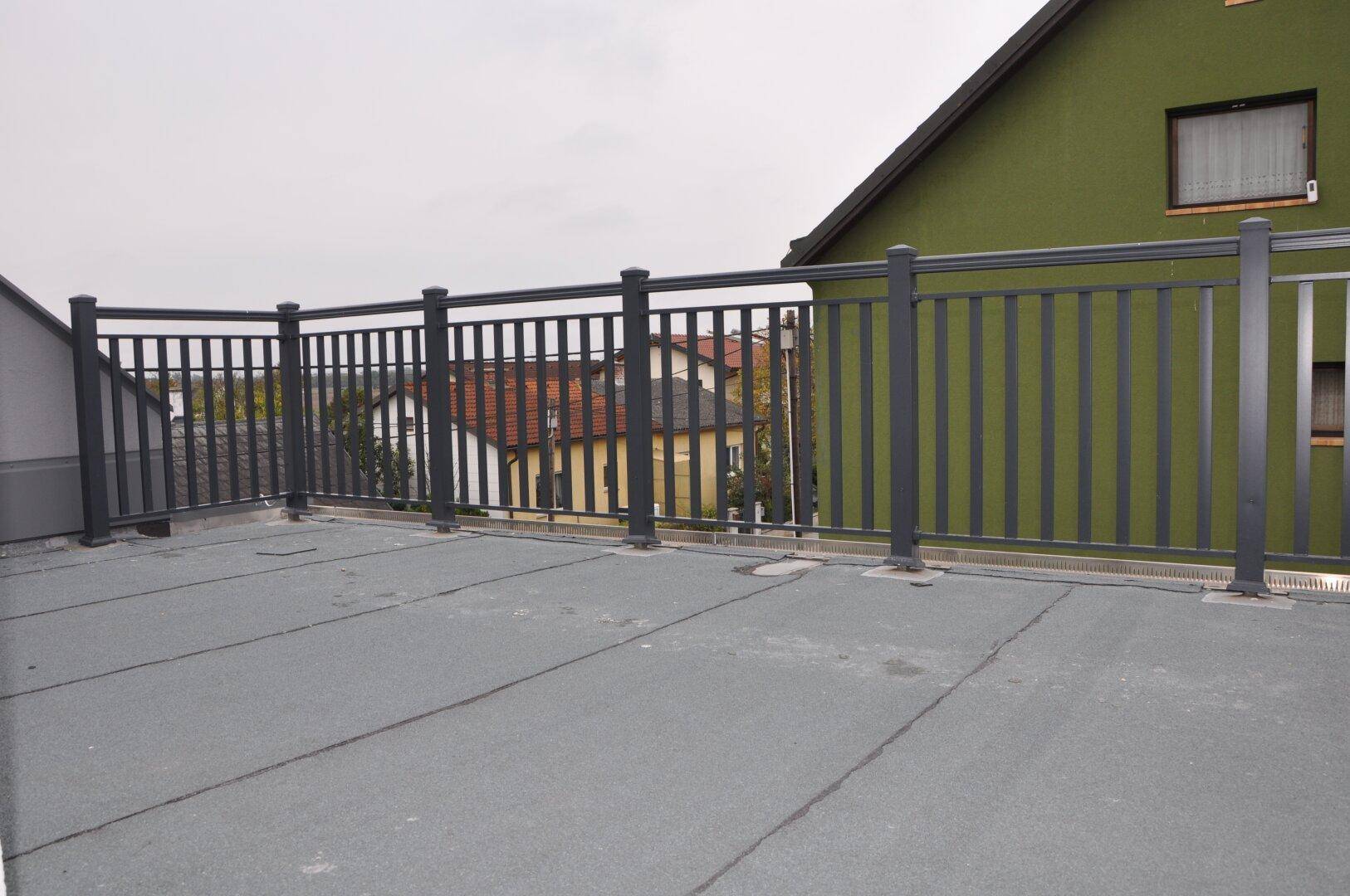 Leere Dachterrasse mit grauem Bodenbelag und Metallgeländer, bereit zur Gestaltung.
