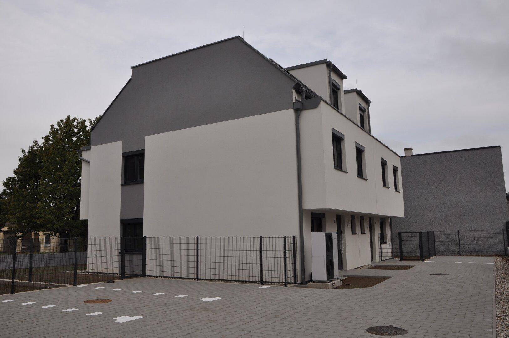 Seitenansicht eines modernen Reihenhauses mit gepflastertem Parkplatz und Zaun.