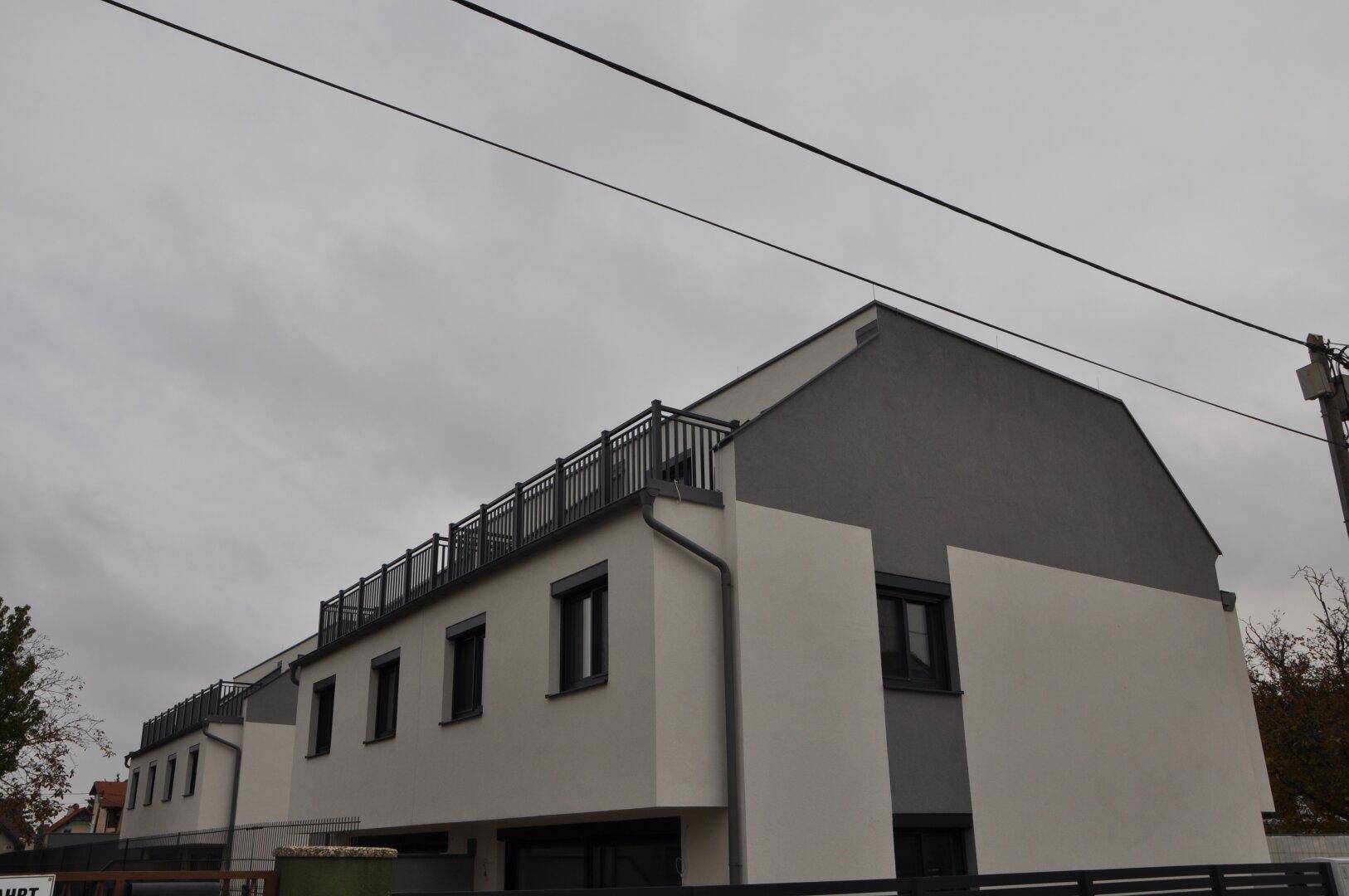 Ansicht eines modernen Reihenhauses mit Flachdach und Dachterrasse unter bewölktem Himmel.