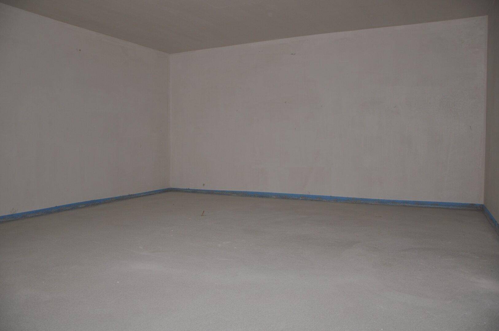 Leerer Raum im Neubau mit unfertigen Wänden und Estrichboden.