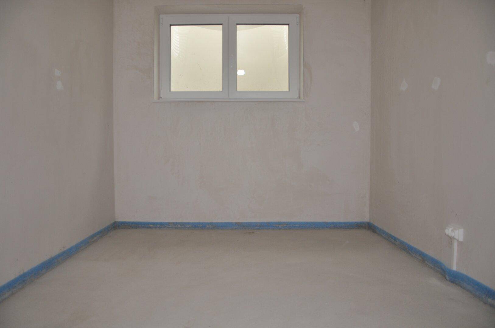 Unfertiger Raum im Neubau mit Fenster und vorbereitetem Boden.