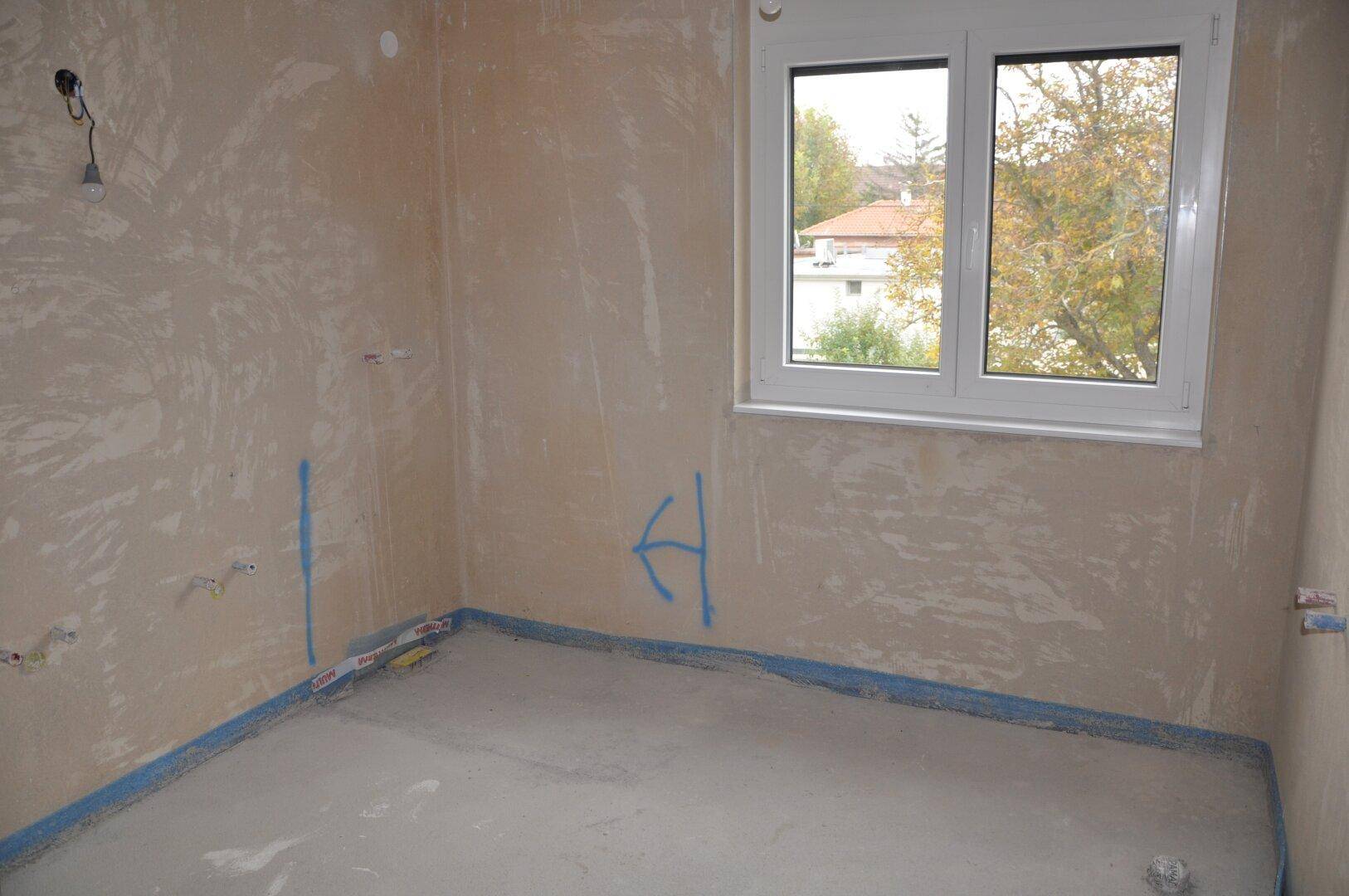 Rohbauraum mit Fenster und sichtbaren Installationen für Sanitär oder Küche.