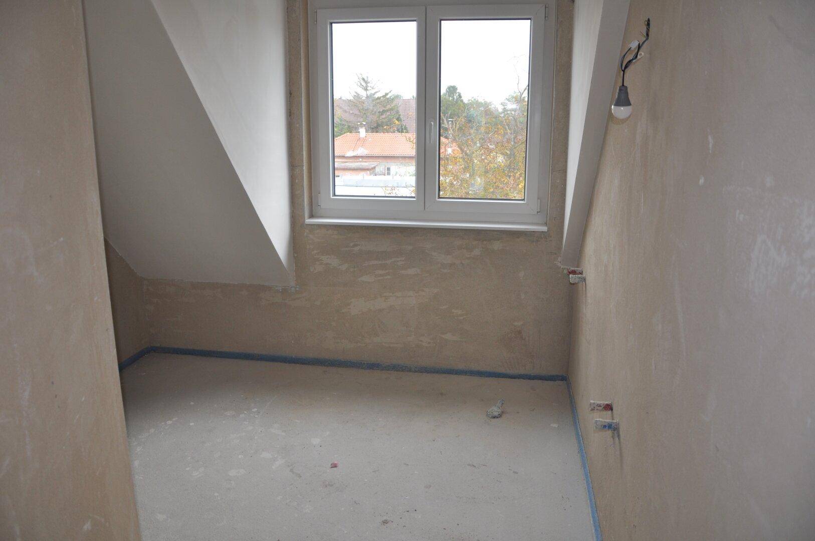 Rohbauraum im Dachgeschoss mit schräger Decke und Fenster.