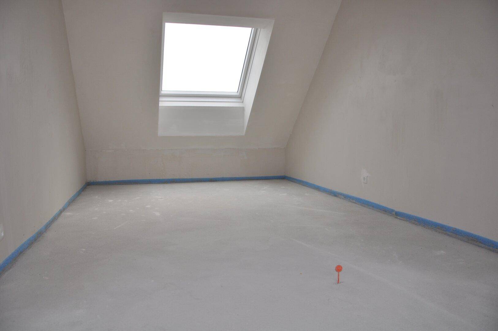 Rohbauraum im Dachgeschoss mit Dachfenster und schräger Decke.