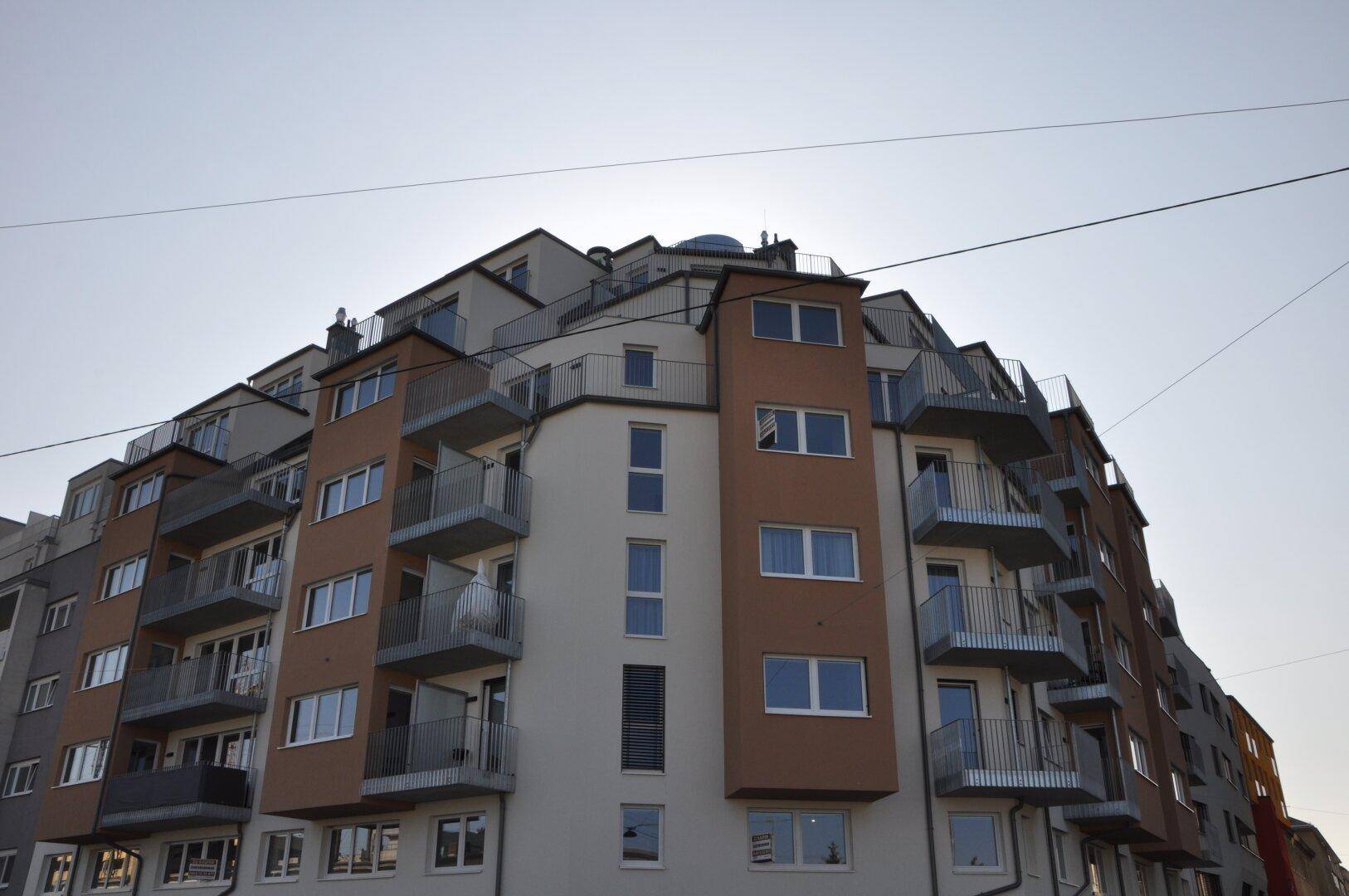 Modernes Mehrfamilienhaus mit vielen Balkonen und gestufter Dacharchitektur unter klarem Himmel.