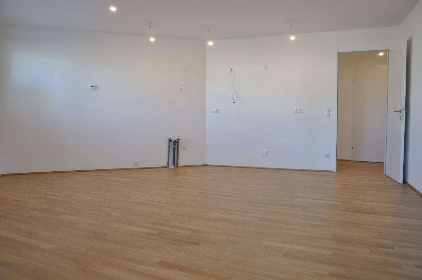 Geräumiger, heller Raum mit Parkettboden und Anschlüssen für eine moderne Küche.
