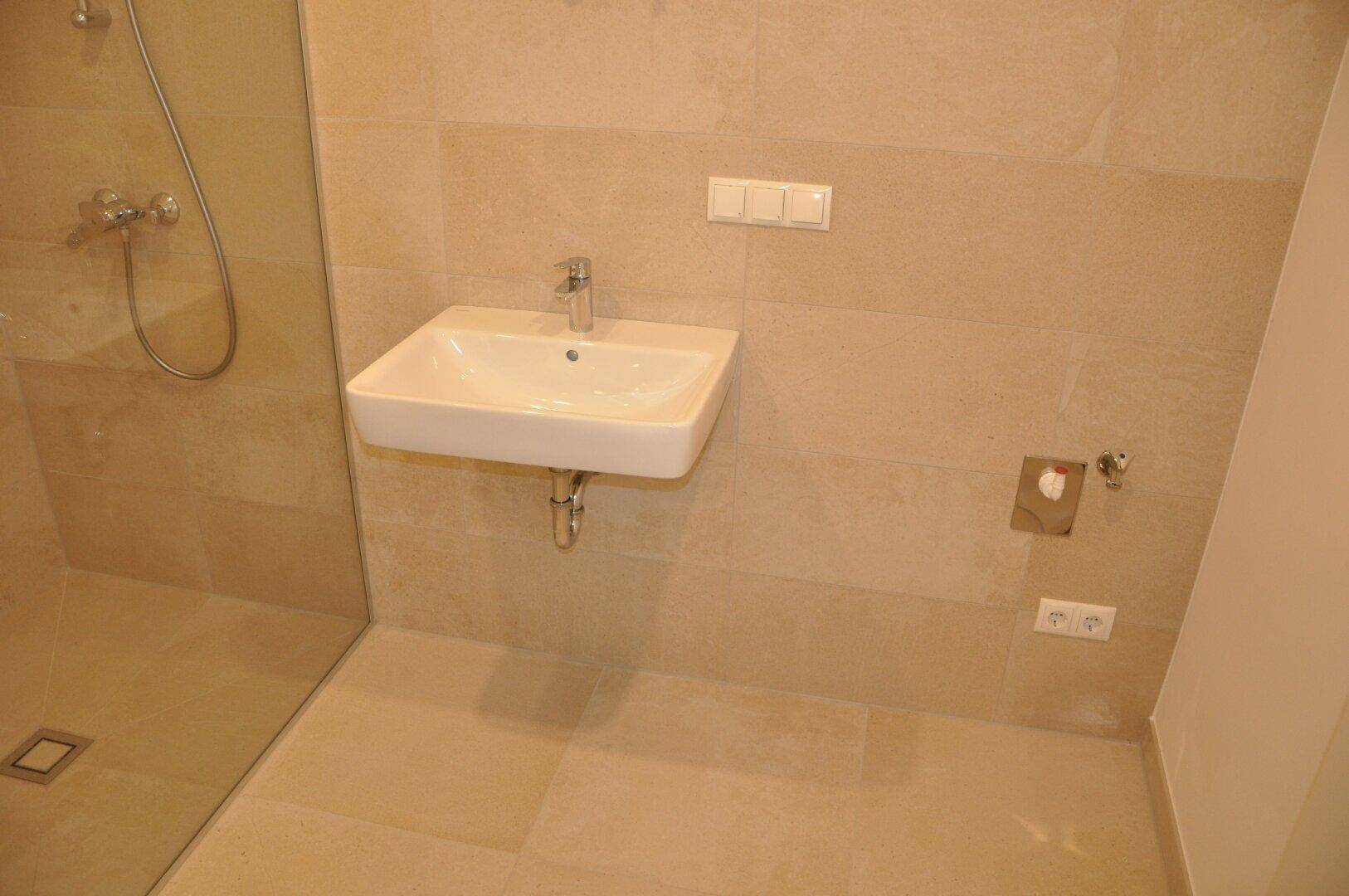 Detailansicht des modernen Waschbeckens und der beigefarbenen Fliesen im Badezimmer.