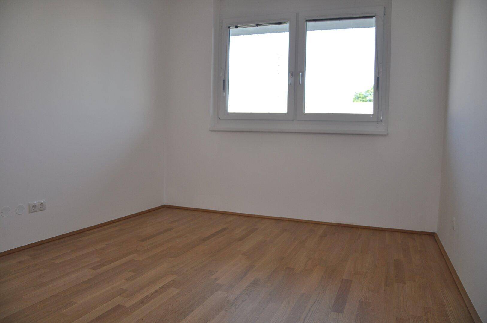 Helles Schlafzimmer mit Parkettboden und einem Fenster, bietet viel Potenzial für persönliche Einrichtung.