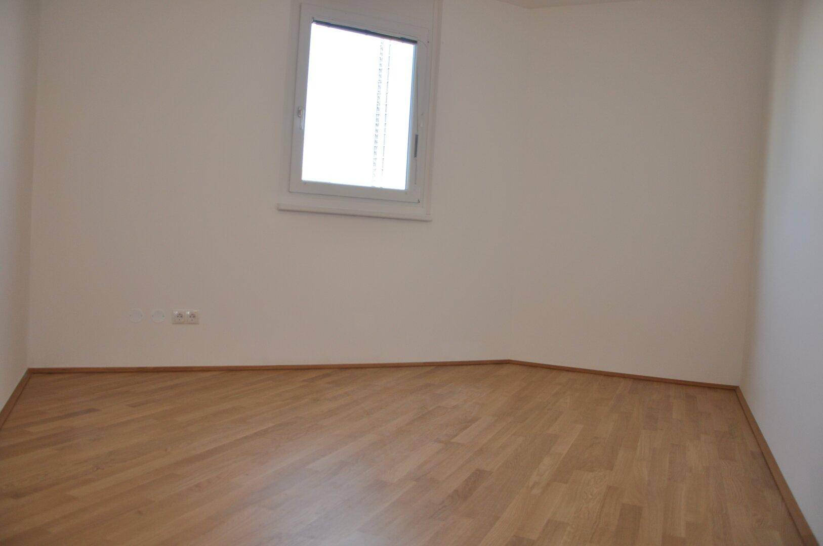 Weiteres helles Schlafzimmer mit Parkettboden und einem Fenster, ideal als Kinder- oder Gästezimmer.