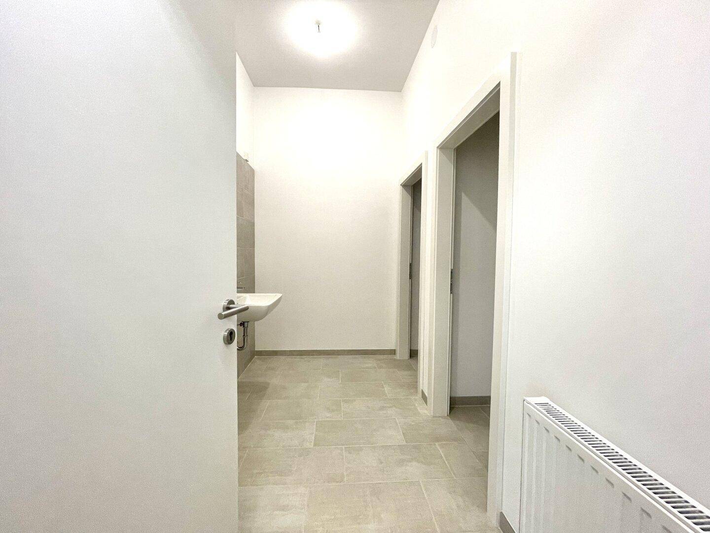 Heller Flur mit gefliestem Boden, der zu mehreren Toilettenräumen führt.