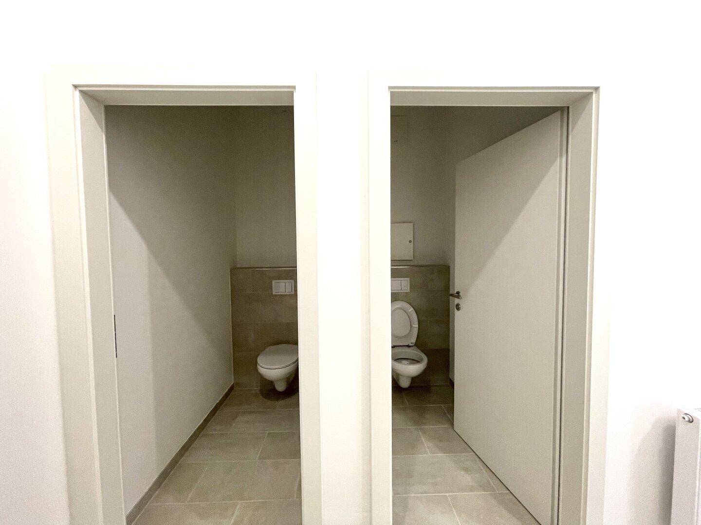 Zwei separate Toilettenkabinen mit Wand-WCs und modernen Fliesen.