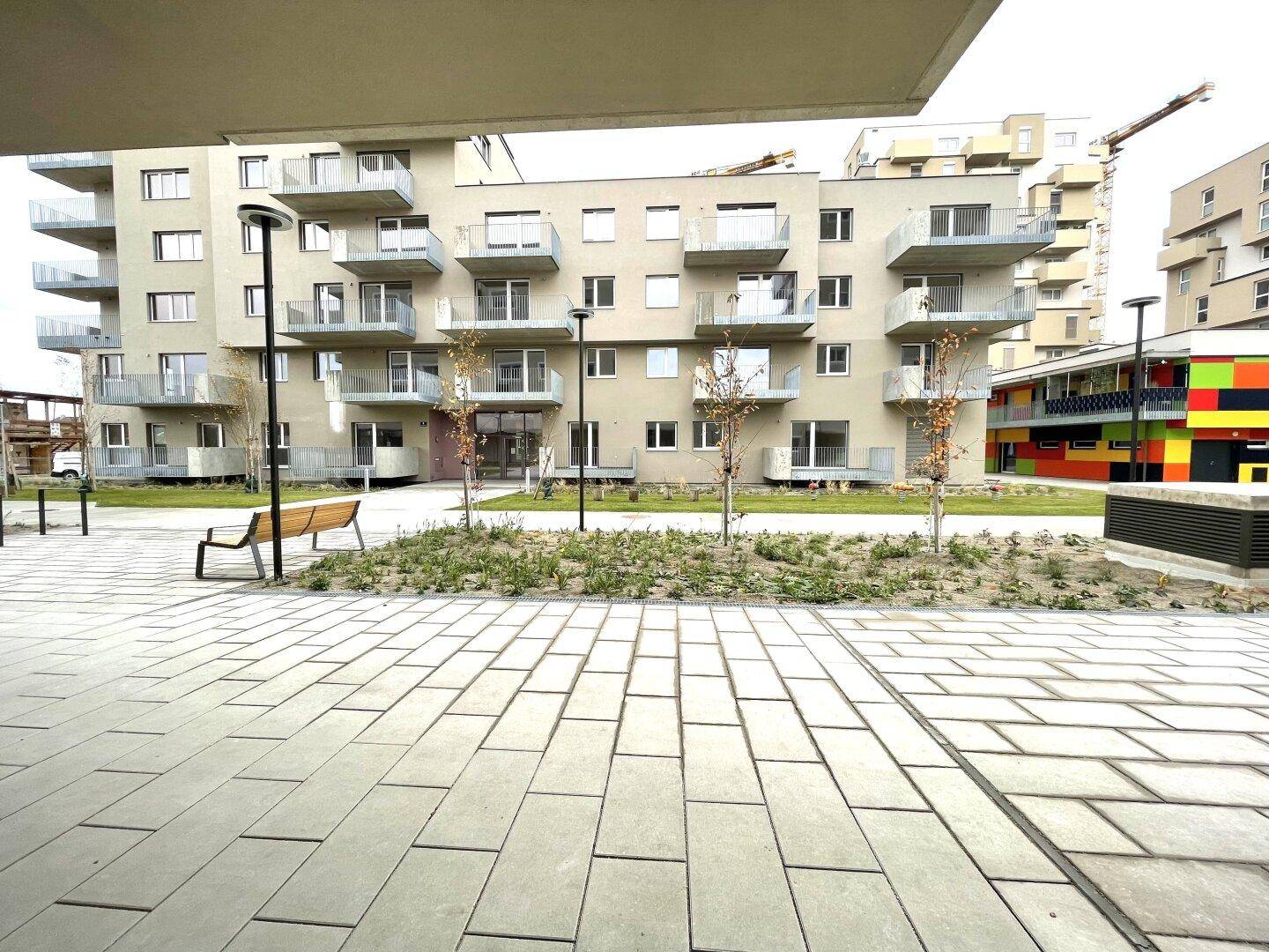 Moderner Wohnkomplex mit Balkonen, einem gepflasterten Innenhof und Sitzgelegenheiten.