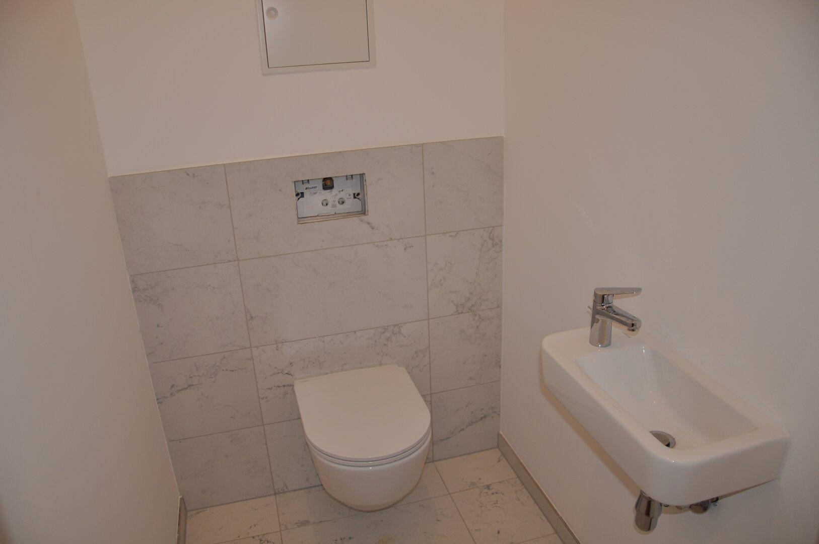 Modernes Gäste-WC mit wandhängender Toilette und kleinem Waschbecken, hell gefliest.