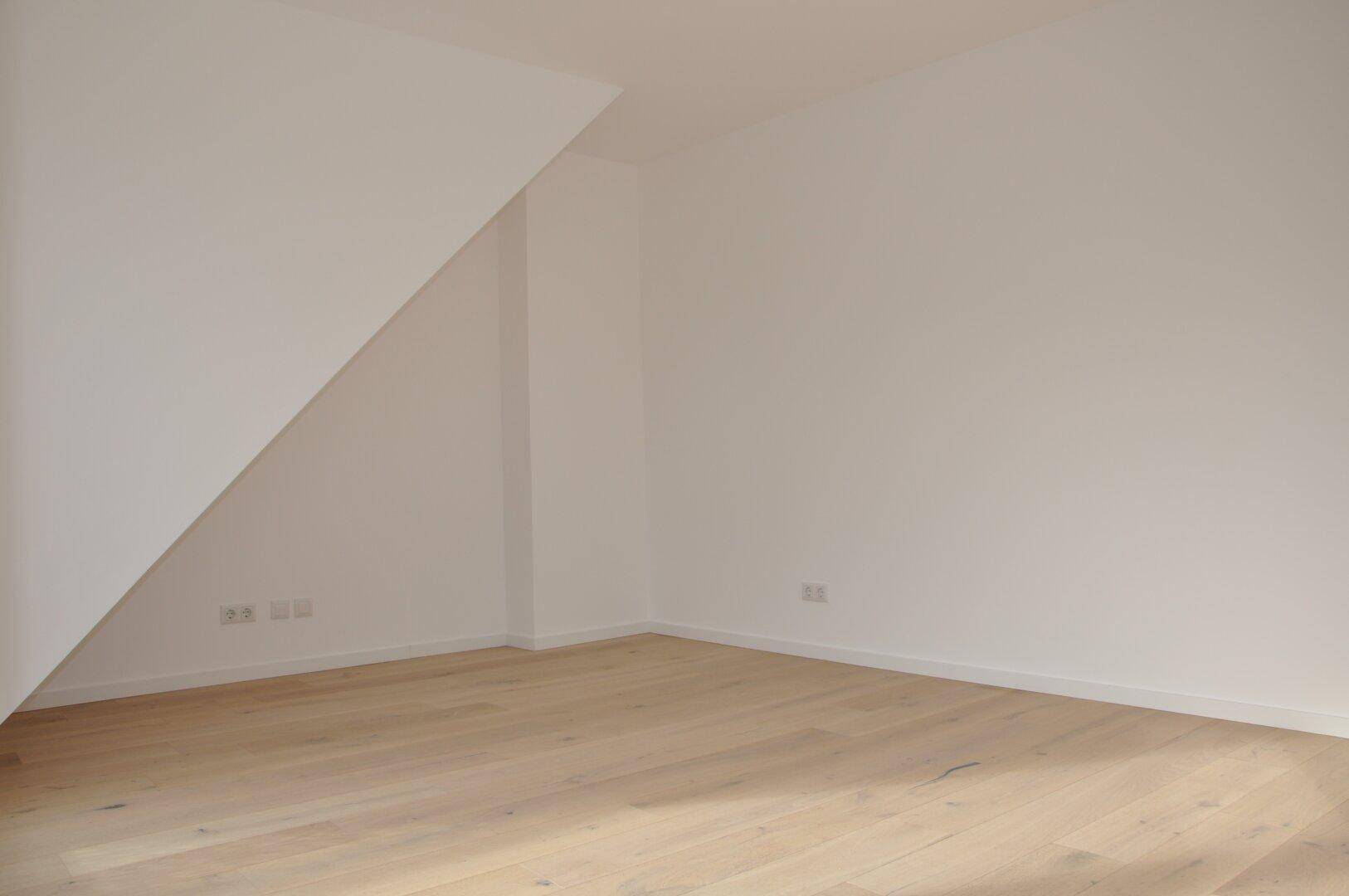 Geräumiges Schlafzimmer mit hellem Holzboden und schrägen Wänden im Dachgeschoss.