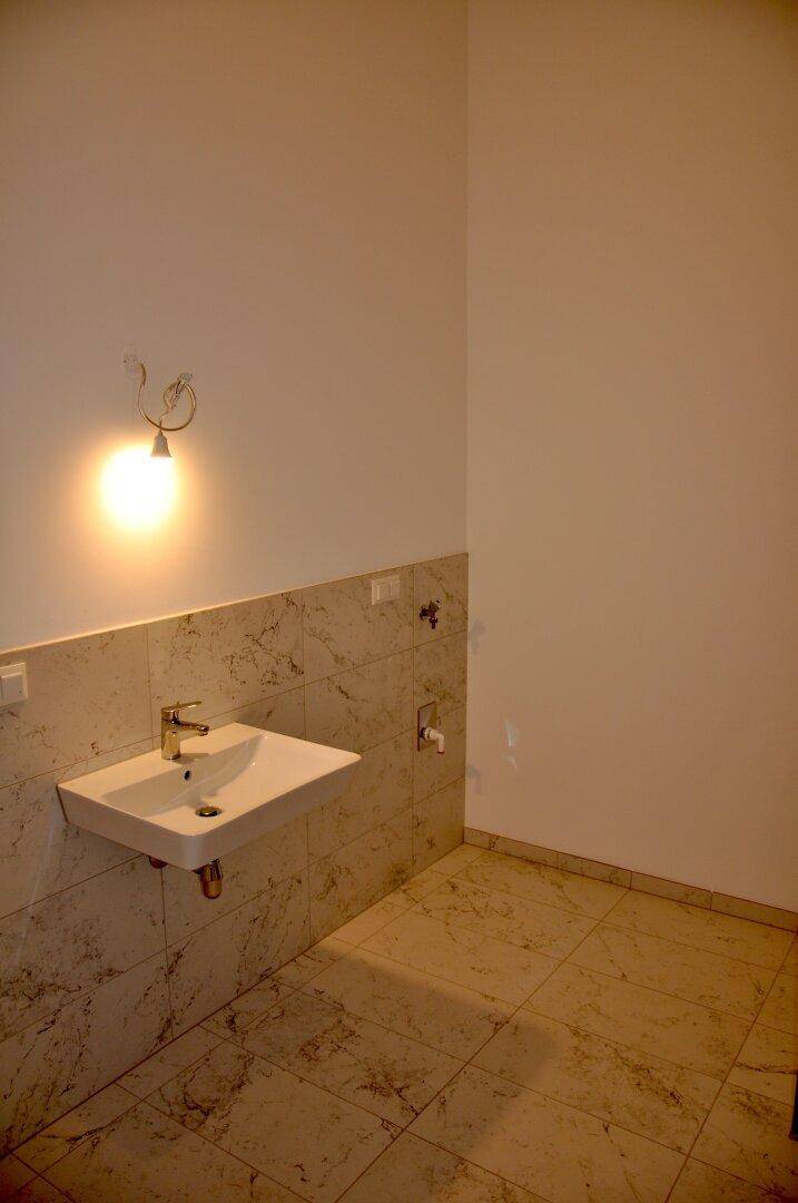 Modernes Badezimmer mit Einzelwaschbecken und hellen Fliesen an Wänden und Boden.