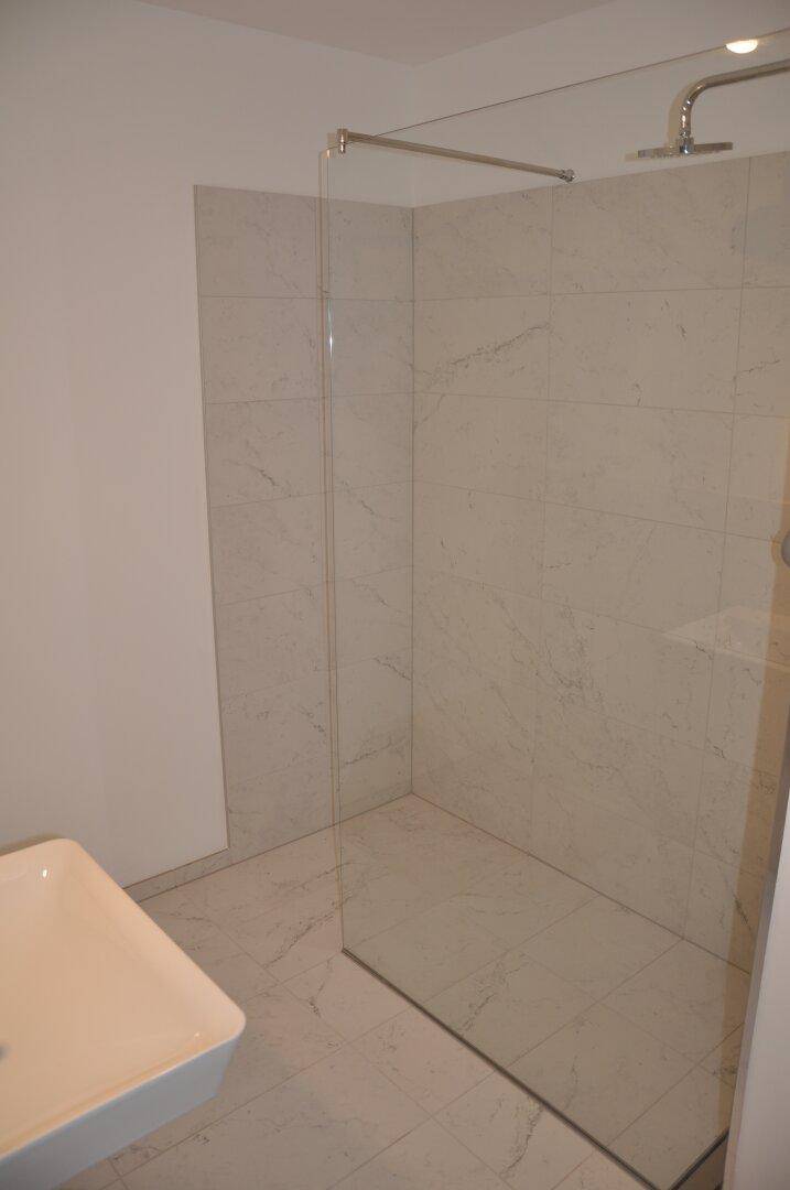 Modernes Badezimmer mit begehbarer Dusche, weißen Fliesen und minimalistischem Design.