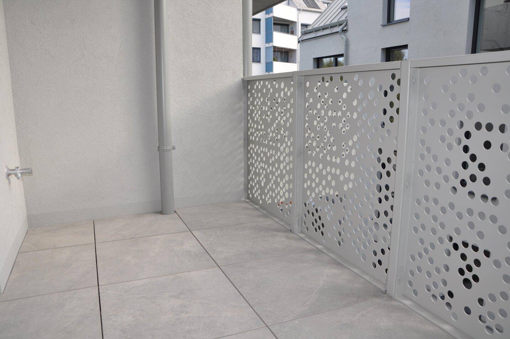 Moderner Balkon mit grauen Fliesen und perforiertem Metallgeländer, bietet Platz im Freien.
