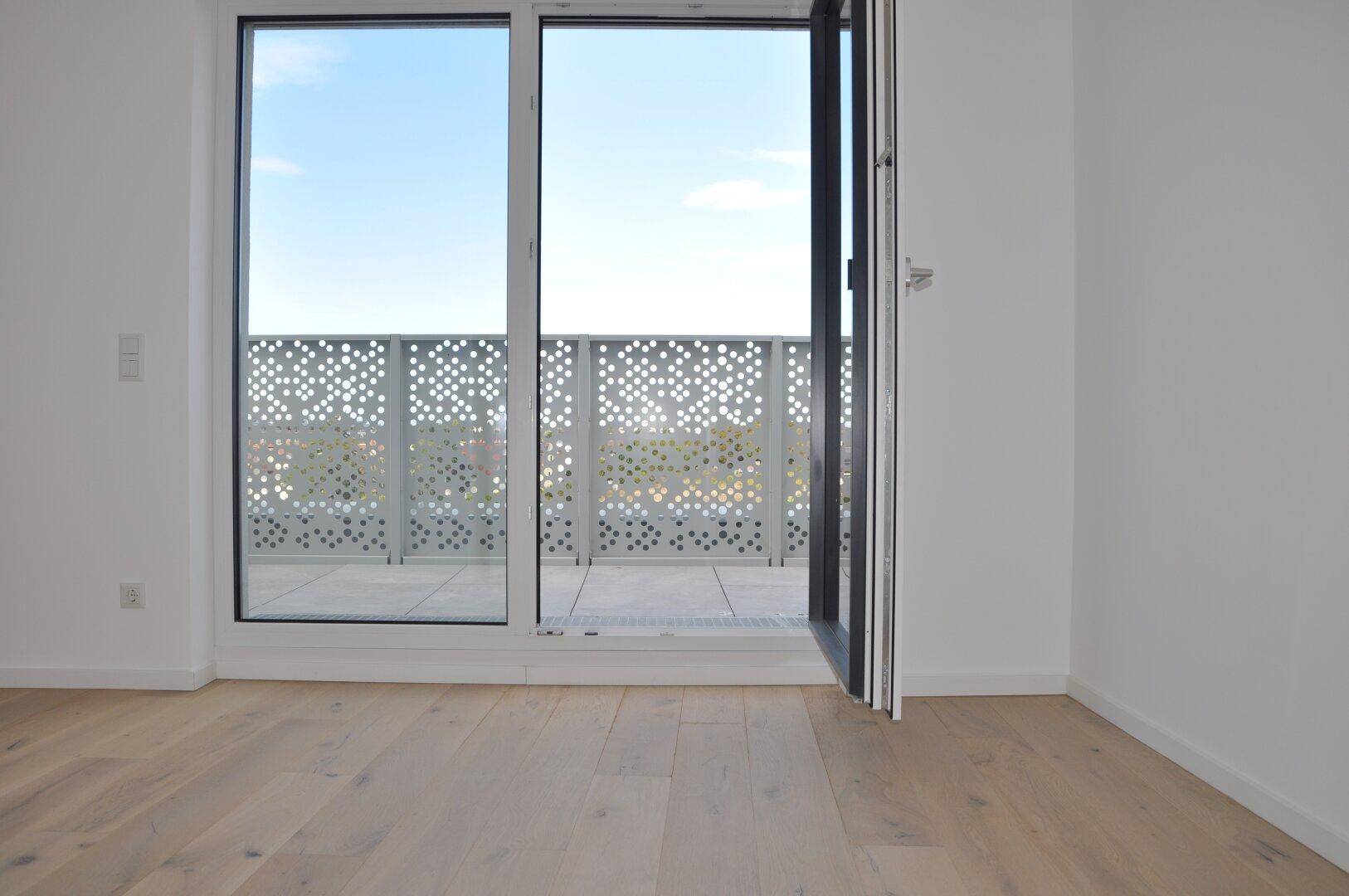 Heller Innenraum mit Holzboden und Zugang zu einer großen Terrasse mit Stadtblick.