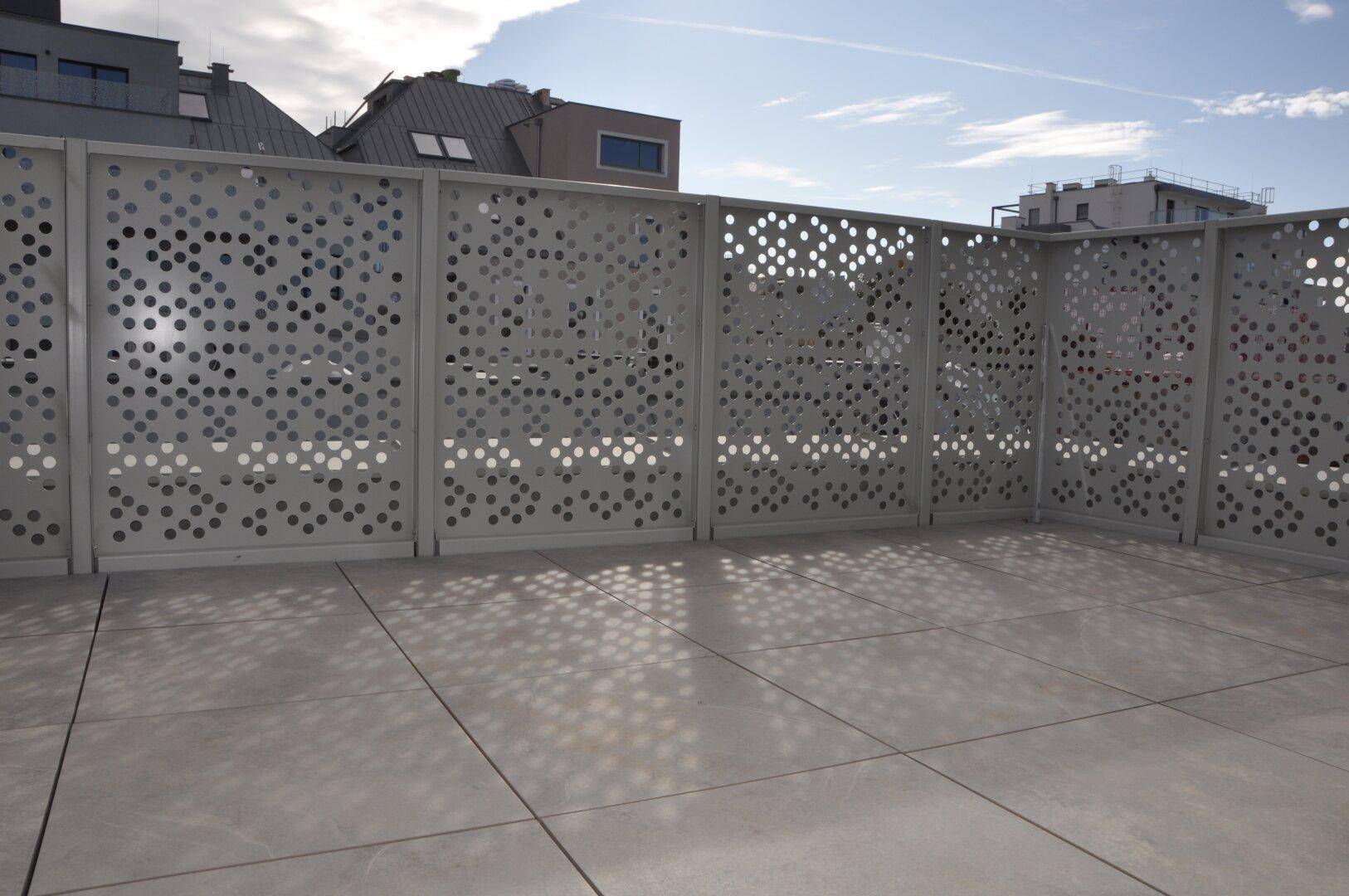 Moderne Terrasse mit Lochblechgeländer und Fliesenboden, die Schattenmuster erzeugt.