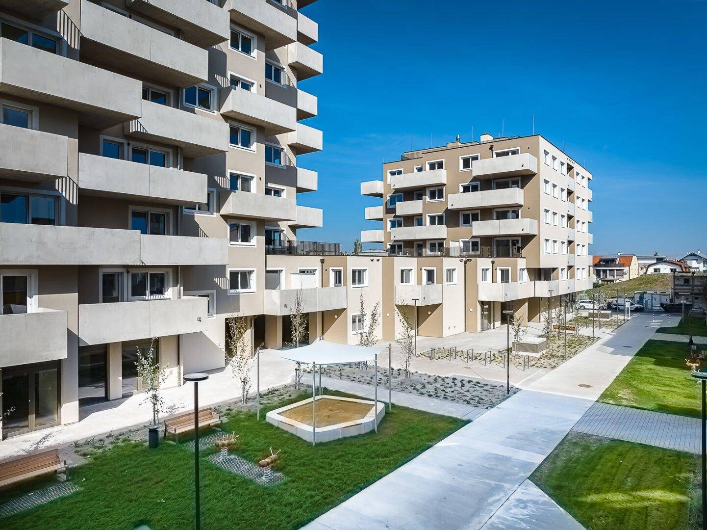 Moderne Wohngebäude mit Balkonen und einem Gemeinschaftsbereich mit Sandkasten und Sitzgelegenheiten.