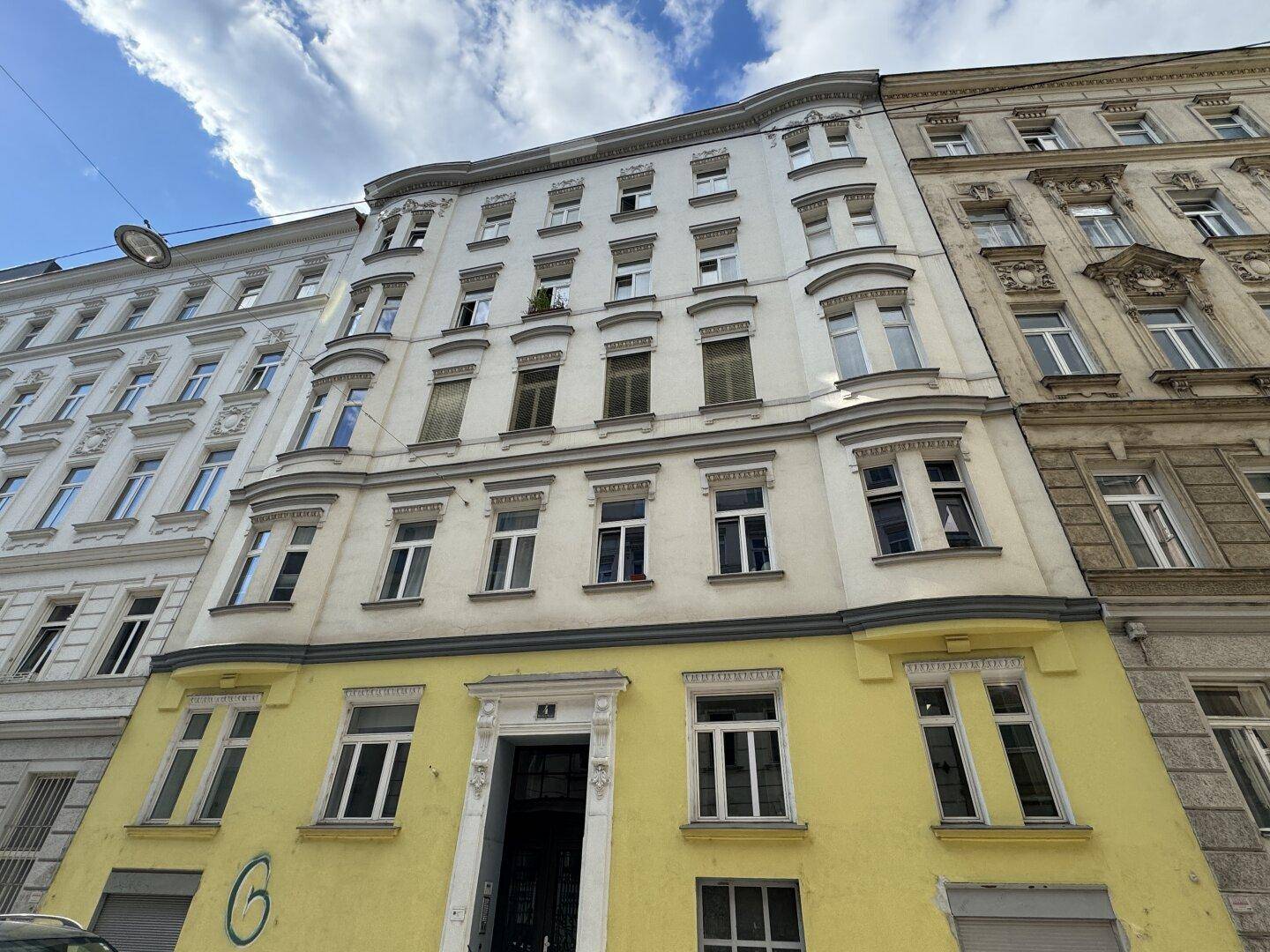 Klassische Altbaufassade mit eleganten Fenstern und einem gelben Sockelbereich unter blauem Himmel.