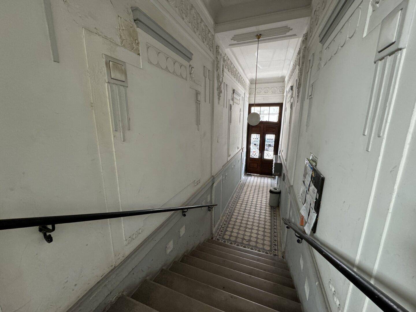 Historisches Treppenhaus mit gemusterten Fliesen, verzierten Wänden und Holzgeländer.