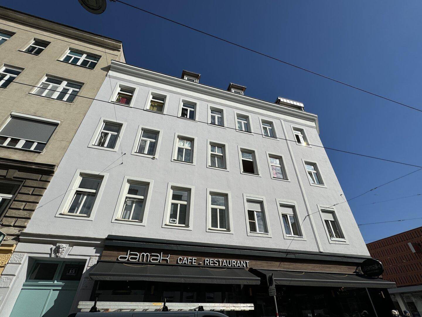 Städtisches Gebäude mit heller Fassade und Rollläden, von der Straßenseite aus gesehen.