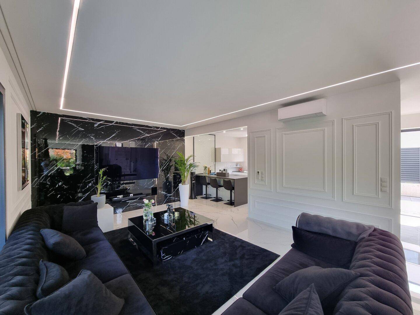 Offener Wohnbereich mit schwarzem Sofa und Blick auf die moderne Küche mit Barhockern.
