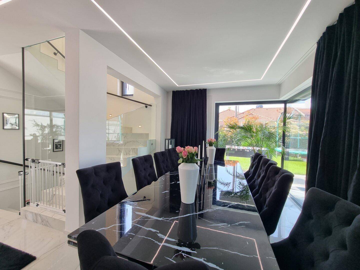Moderner Essbereich mit Marmortisch und Blick auf die elegante Glas-Marmortreppe.