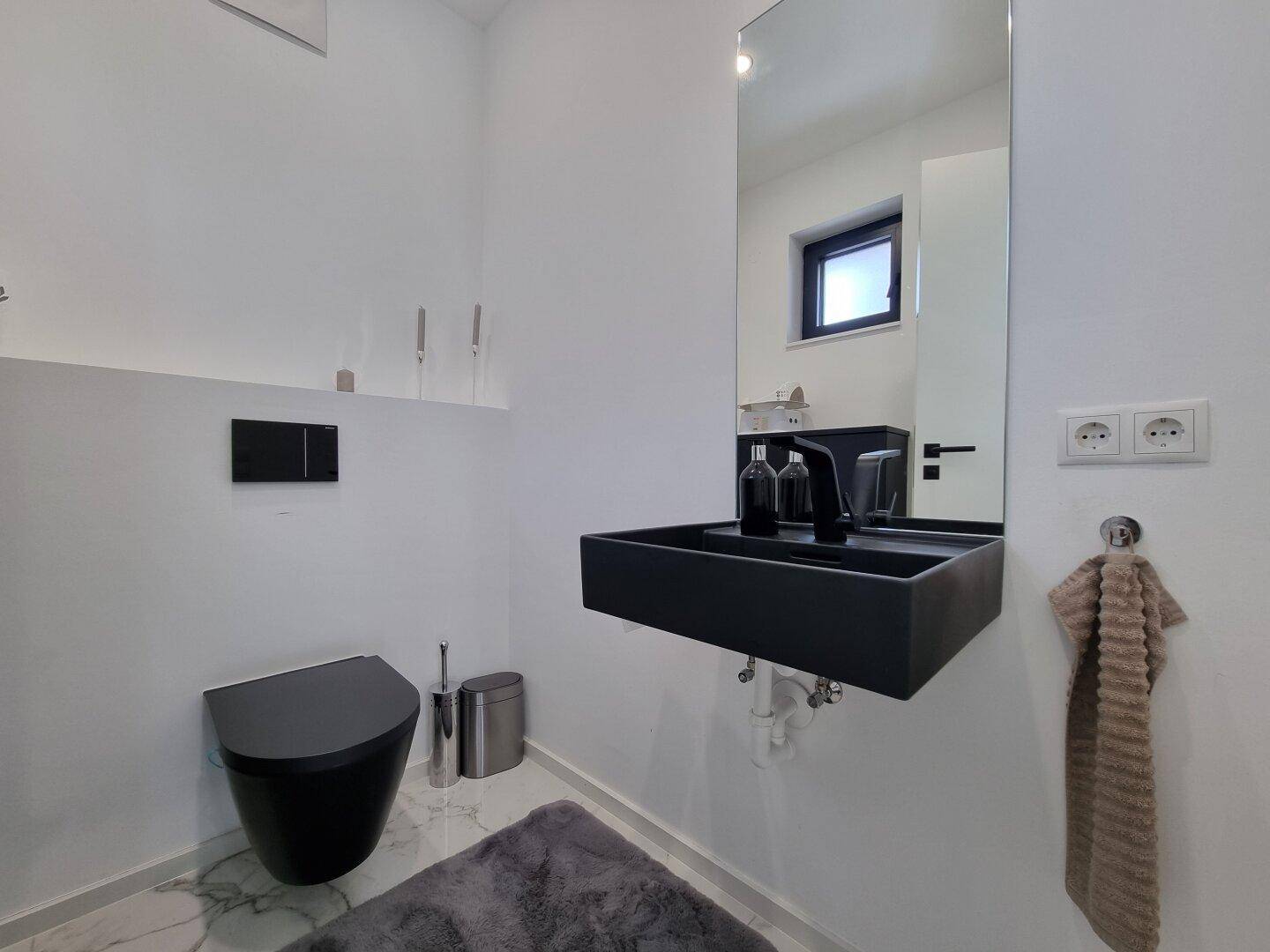 Modernes Gäste-WC mit schwarzer Toilette, schwarzem Waschbecken und großem Spiegel.