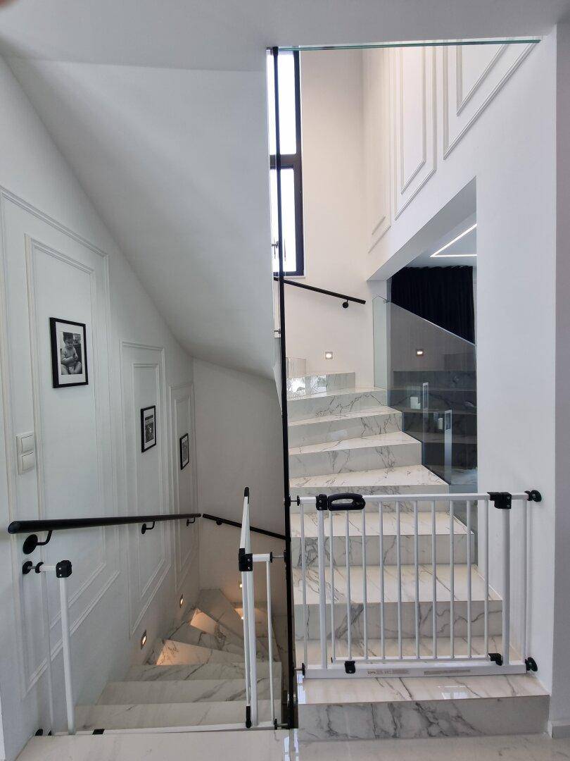 Elegante Treppe mit Marmorstufen, Glasgeländer und weiß getäfelten Wänden.
