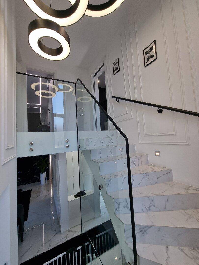 Moderne Treppe mit Marmorstufen, Glasgeländer und stilvollen runden Hängeleuchten.