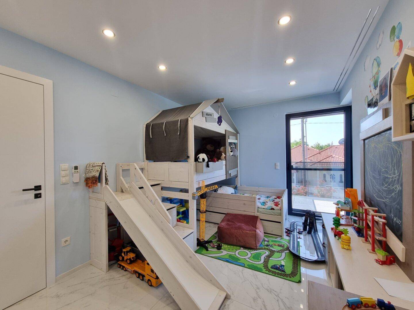 Farbenfrohes Kinderzimmer mit Spielbett, Rutsche, blauen Wänden und vielen Spielsachen.