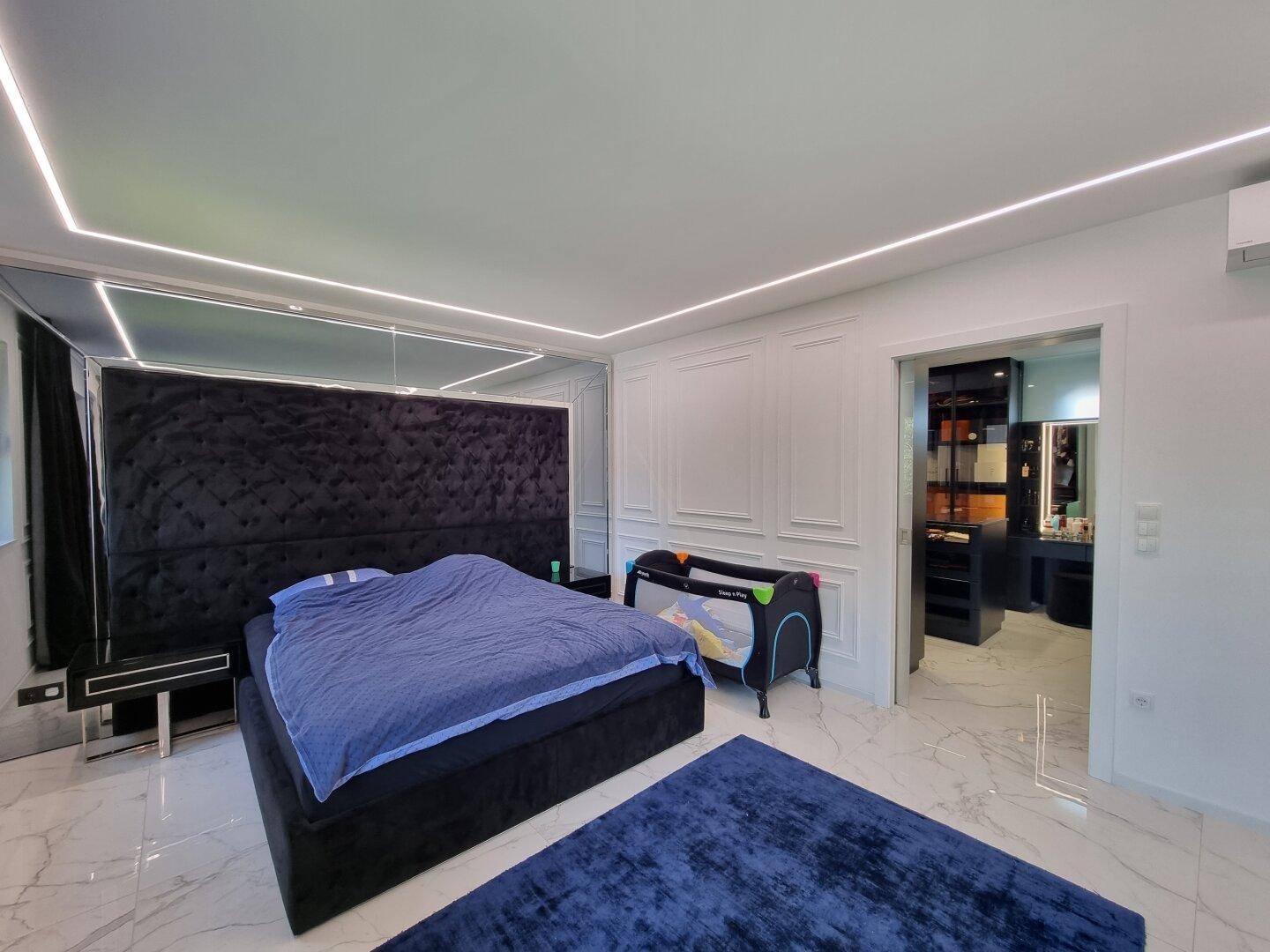 Elegantes Schlafzimmer mit großem Bett, Babybett und direktem Zugang zum begehbaren Kleiderschrank.