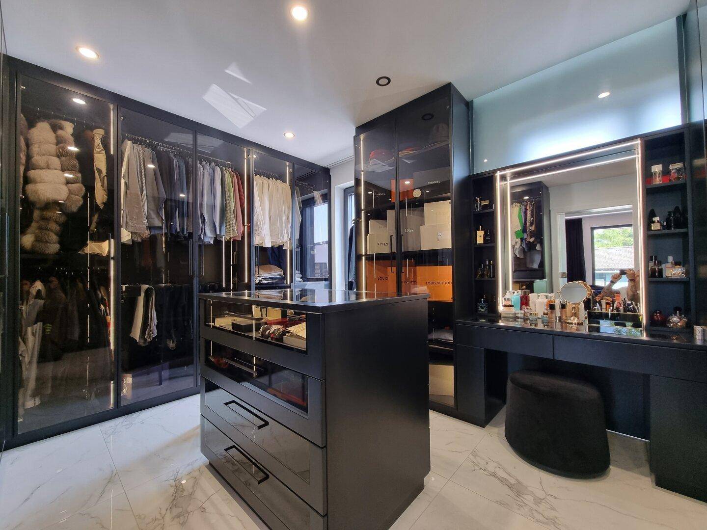 Luxuriöser begehbarer Kleiderschrank mit schwarzen Glasvitrinen, Mittelinsel und Schminktisch.