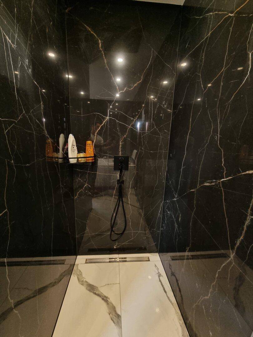 Elegante begehbare Dusche mit schwarzen Marmorfliesen und minimalistischem Design.