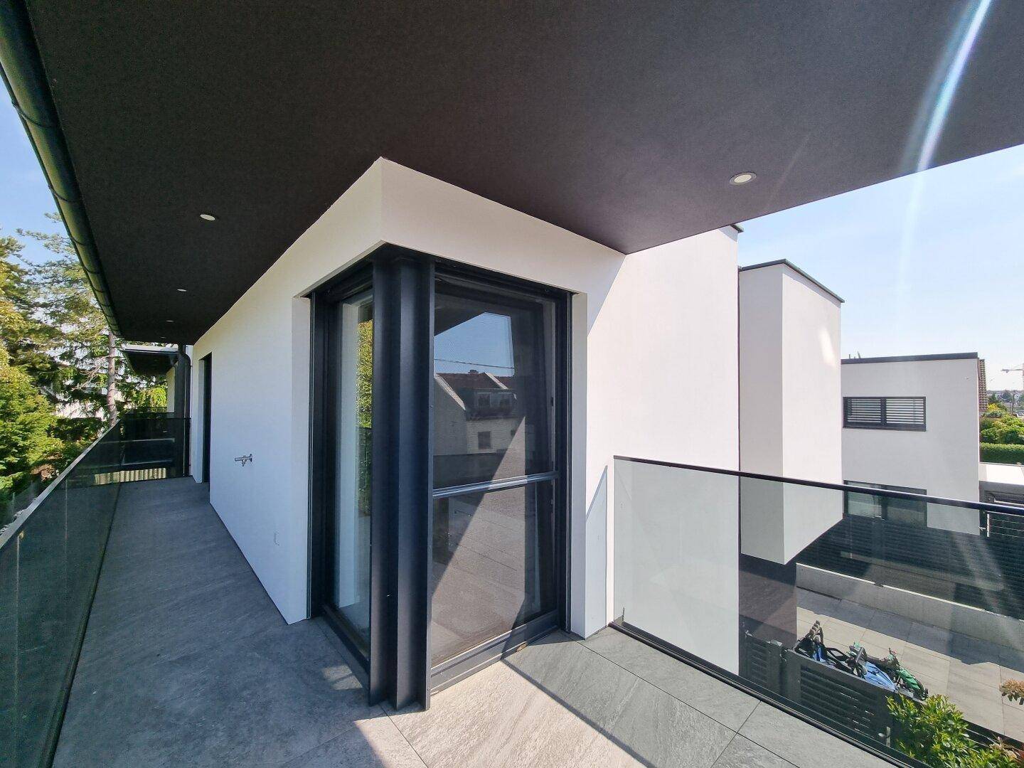 Moderne Terrasse mit Glasgeländer und Blick auf die Umgebung, ideal für Entspannung im Freien.