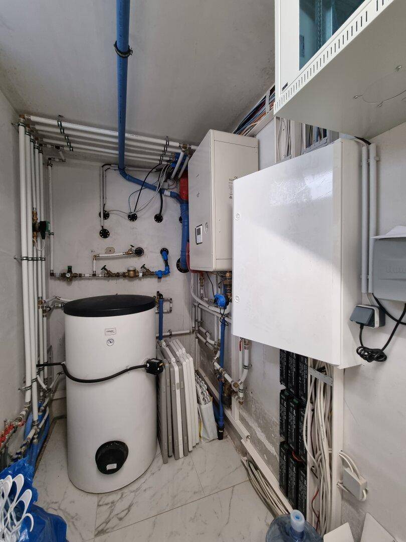 Technikraum mit Heizungsanlage, Warmwasserspeicher und sichtbaren Installationen.