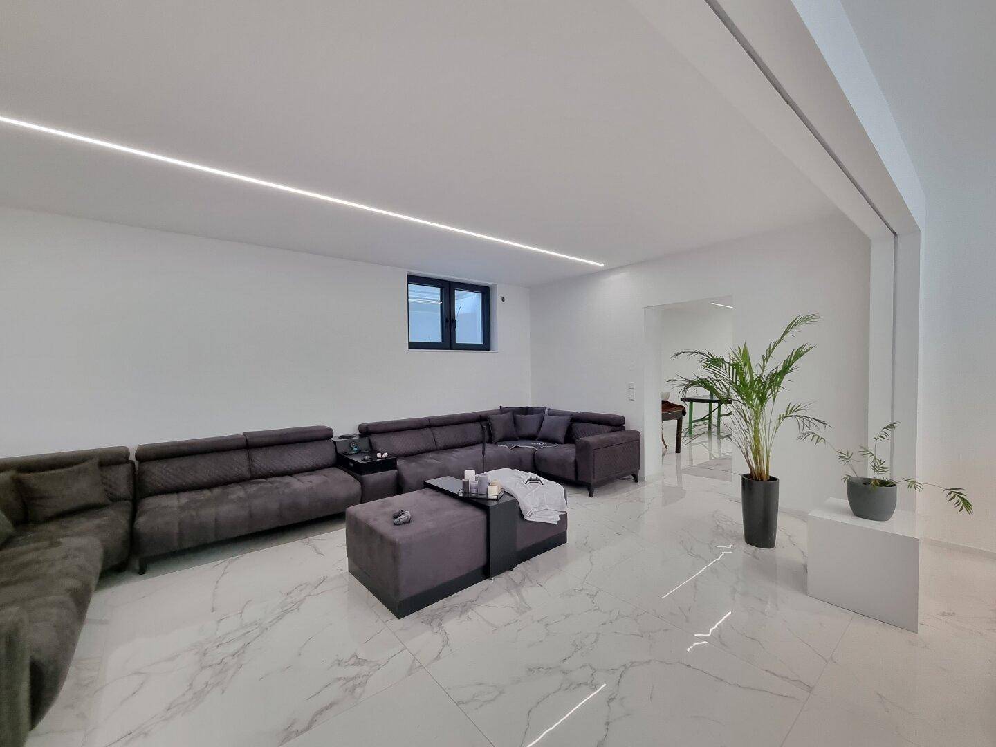 Geräumiges Wohnzimmer mit großem Ecksofa, minimalistischer Einrichtung und glänzendem Boden.