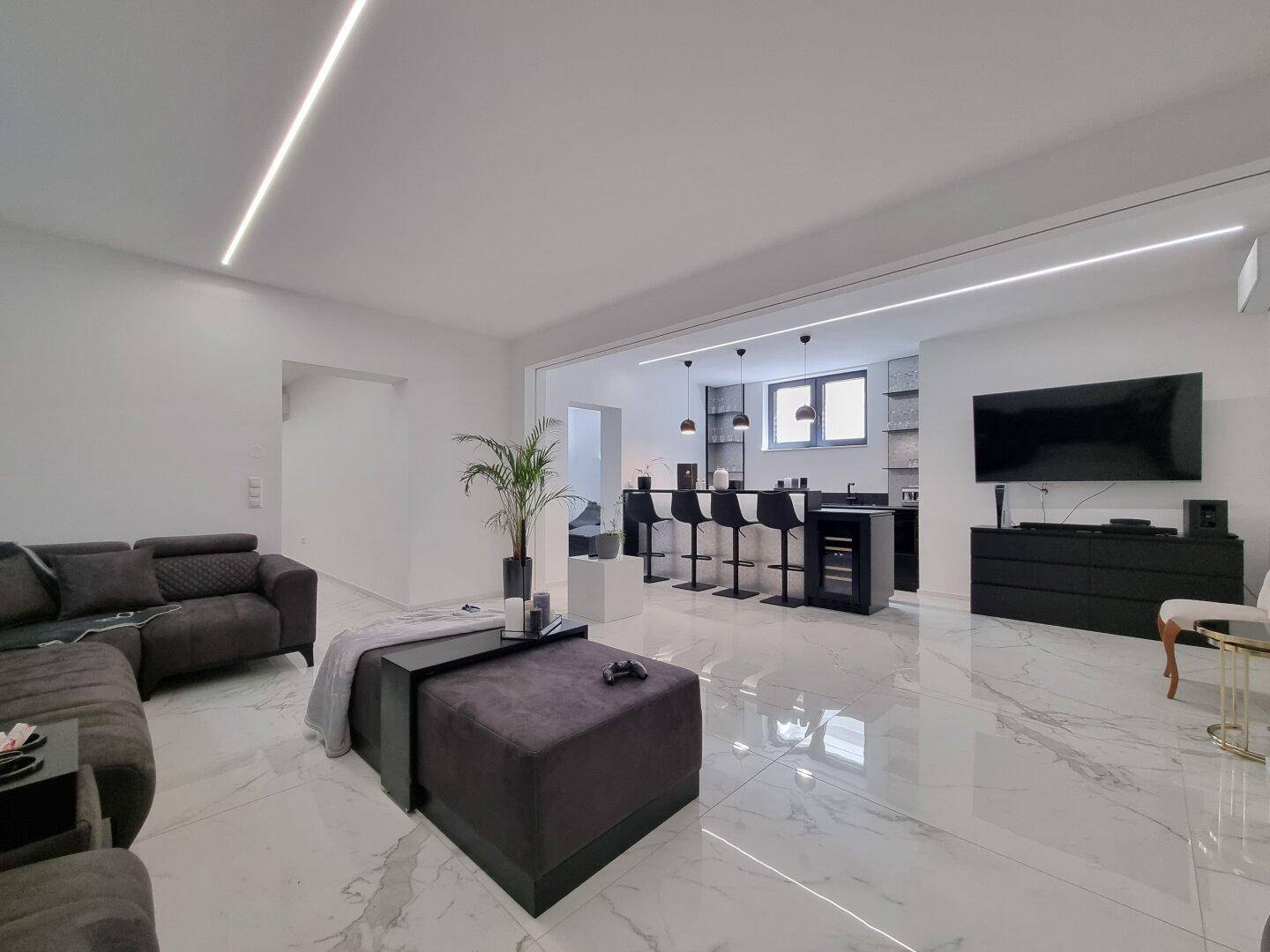 Moderner offener Wohnbereich mit dunklem Sofa, Bar und glänzendem Marmorboden.