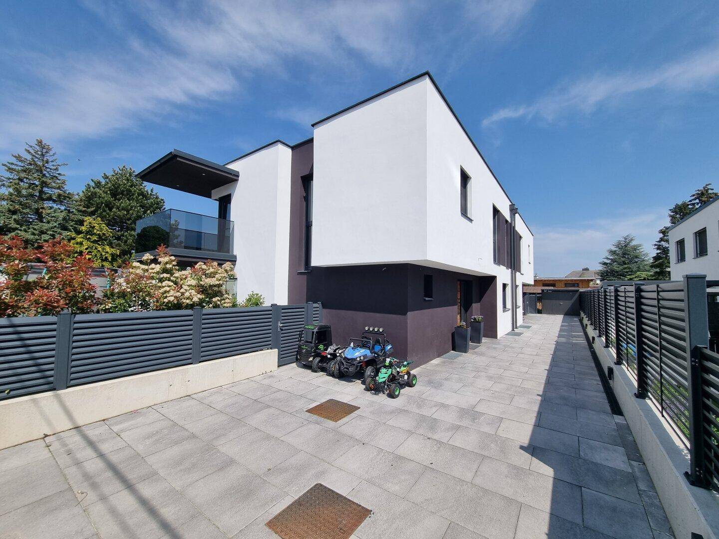 Moderne Architektur des Neubaus mit weißer und dunkler Fassade sowie gepflasterter Zufahrt.